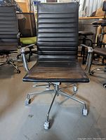 Front view of black Eames style office chair showing ribbed faux leather seat and backrest, chrome armrests and base with caster wheels.