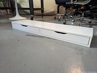 White Ikea Alex shelf low profile with two drawers closed, sitting on floor in office setting.