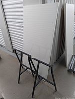 White rectangular Ikea desktop leaning vertically with visible marks and stains. Black metal sawhorse leg framework resting in front.