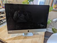 Front view of silver Apple iMac on wooden table, screen off