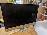 Front view of iMac desktop computer with black screen, aluminum stand and base, sticker FR-201612-DO on lower bezel