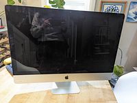 Front view of silver Apple iMac all-in-one computer on wooden table, display off.
