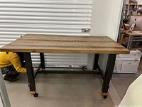 Side view of assembled table showing reclaimed wood surface and black metal legs with casters.