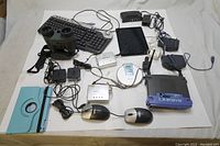 Top-down view of all items including binoculars, keyboard, mice, router, iPad, CD player, and Wi-Fi adapters spread out on white background.