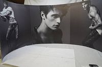 Curved black-and-white vinyl banner showing three images of the same young male model, shirtless in poses showcasing physique.