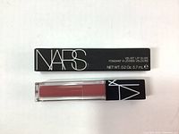 NARS Velvet Lip Glide lip gloss and packaging showing front view of product and box with branding and product details.