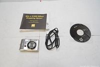 Nikon Coolpix L19 digital camera with USB cable, software CD, and promotional booklet laid out on a white surface, showing included accessories.