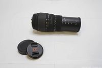 Side view of black Sigma telephoto zoom lens showing zoom and focus rings and removable lens caps with Sony Alpha logo.