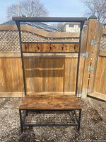 Front view of coat rack bench showing wood veneer surfaces and black metal frame with five hooks.