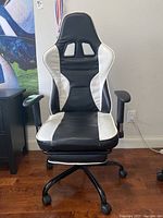 Front view of black and white gaming chair showing padded seat, backrest with cut-out sections, and adjustable armrests.