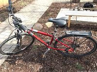 Full view of the red Gary Fisher bicycle with black back rack and kickstand, showing overall condition including frame, wheels, and pedals.