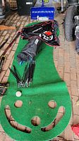 Full view showing golf putting green mat with multiple hole cutouts, mesh net poles, and driving net in bag.