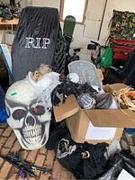 Photo showing large skull decoration with red LED eyes and fabric coffin with RIP embroidery, along with styrofoam tombstones and assorted props in boxes and bags.