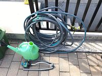 Photo showing the green plastic watering can, coiled grey garden hose with blue fittings and brass connectors, and Yardworks oscillating sprinkler.