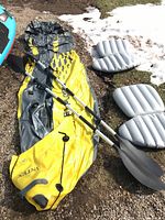 Deflated yellow and gray kayak laid out on ground with two paddles and two inflatable seats