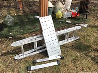 Folded aluminum ladder laid on grass with work platform panel and two rubber feet attachments.