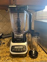 Full view of Ninja Professional Blender with large pitcher and two personal cups with lids on kitchen counter.