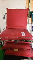 Stack of four outdoor cushions with red fabric face and visible ties on side.
