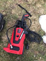 Photo showing the full pressure washer on grass, highlighting the hose, power cord, and overall unit condition.