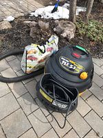 Front view of QPV Shop Vac with hose and colorful reusable bag in background on brick patio.