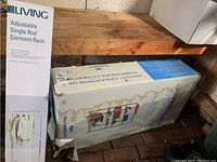 Photo showing unopened For Living Adjustable Single Rod Garment Rack box standing vertically on a wooden surface.