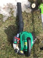 Top view of green Weed Eater gas leaf blower laying on grass showing black handle, fuel tank, and air vent.