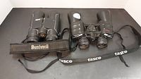 Two pairs of binoculars side by side, Tasco on the right and Bushnell on the left.
