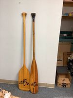 Front view of two 60-inch wooden canoe paddles with eagle design on one paddle's blade and plain on the other.