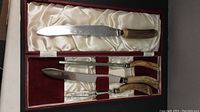 Full set of bone-handled carving utensils including a larger knife, two additional knives, and two-prong fork set in a red velvet lined box with cream satin interior.