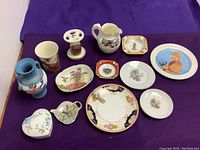 Overview of all items laid out on purple fabric showing vases, plates, ashtrays, and decorative items with floral and bird themes.