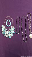 Five stone and bead jewelry pieces arranged on purple background, including necklaces and one bracelet.