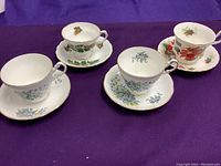 Four porcelain cups and saucers displayed on purple fabric, showing variety of floral patterns and colors