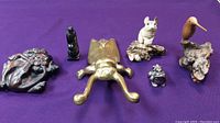 Overview of six animal figurines on purple background, including brass frog, brass beetle, wooden bird, cream-colored animal, small black figurine, and carved brown piece.