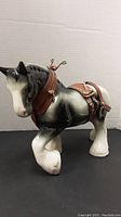 Side view showing black and white ceramic horse with brown leather harness and metal accents