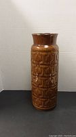 Front view of tall cylindrical brown ceramic vase with geometric textured pattern.