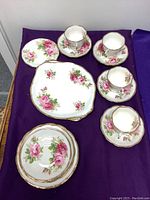Overview of cups, saucers, small and medium plates showing floral pattern and gold trim on white porcelain.