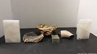 All items in lot shown on black and white background including alabaster bookends, petrified wood, fossil, and stones