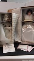 Photo showing two boxed porcelain dolls Winter Romance and Finishing Touch with Certificates of Authenticity laid out in boxes.