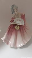 Front view of the Royal Doulton Elaine figurine in a pink and white gown holding a floral fan with hang tag attached.