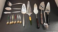 Photo of all the serveware items including 3 cake servers and 6 enamel appetizer spoons.