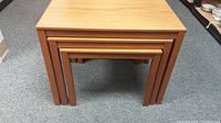 Stacked set of three teak laminate nesting tables showing all three sizes nested within each other.