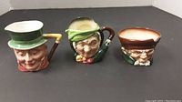 Front view of three Toby character mugs showing faces and colored hats