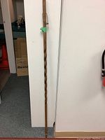 Full length view of the walking stick leaning against a white wall, showing the twisted wooden shaft and overall shape.