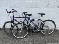 Two bicycles leaning against a white wall, one purple Dragoon and one silver/blue Murray Teewuride.