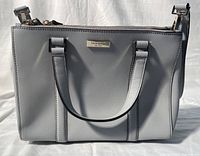 Front view of the grey Kate Spade handbag showing structure, dual handles and logo plaque.