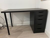 Side view of black IKEA desk showing the surface and one leg, with the five-drawer unit on the right side.