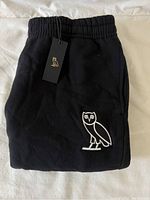 Folded black track pants showing OVO owl logo embroidery and attached brand tag