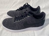 Side view of pair of black Nike Air women's sneakers with white sole, showing textured knit upper and Nike swoosh logo.