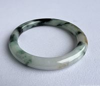 Top side view of the round jade bracelet on white fabric showing smooth polished surface and marbled green and black patterns with some brown inclusions.