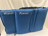 Side by side view of two folded Lightspeed self inflating air mattresses in blue, showing ribbed surface and valve detail.